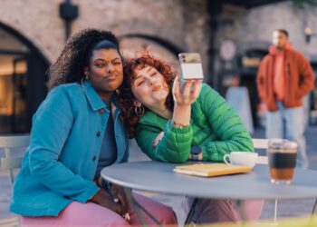 a person taking a selfie with another woman sitting at a table