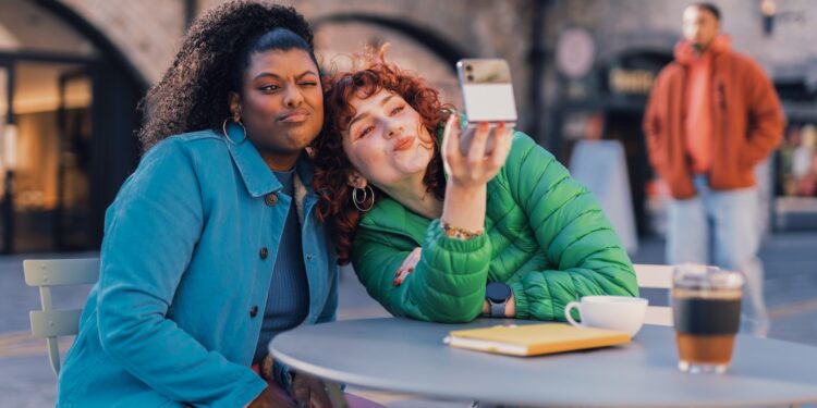 a person taking a selfie with another woman sitting at a table